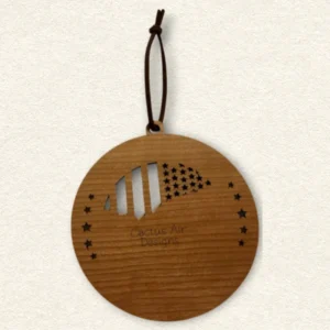 Back of the round wooden ornament showing the natural wood grain, an attached brown hanging cord, and “Cactus Air Designs” laser engraved in a delicate single-line font.