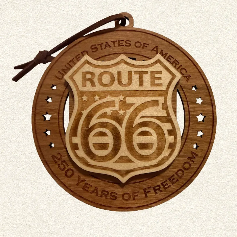 usa-250-route-66-wood-ornament-front • Cactus Air Designs Round layered wooden ornament held in an adult hand for scale, featuring a raised Route 66 highway shield surrounded by star cutouts. The border reads “United States of America” and “250 Years of Freedom.”