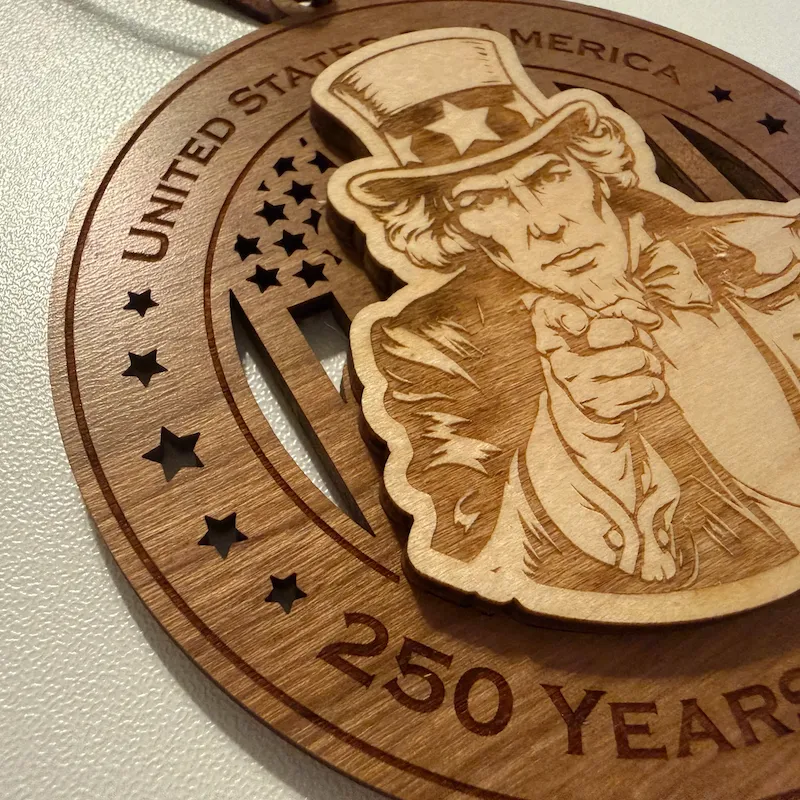 Close-up detail of a layered wooden ornament showing a raised Uncle Sam pointing forward, with laser-engraved facial features, clothing, bow tie, and star-decorated top hat over a cut-through American flag background.