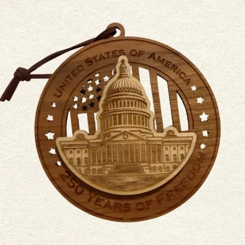 Round two-layer wooden ornament with "United States of America" and "250 Years of Freedom" engraved on the border, featuring a laser-cut flag with cut-through stripes and star field, topped with a detailed US Capitol building, hung on a brown cord