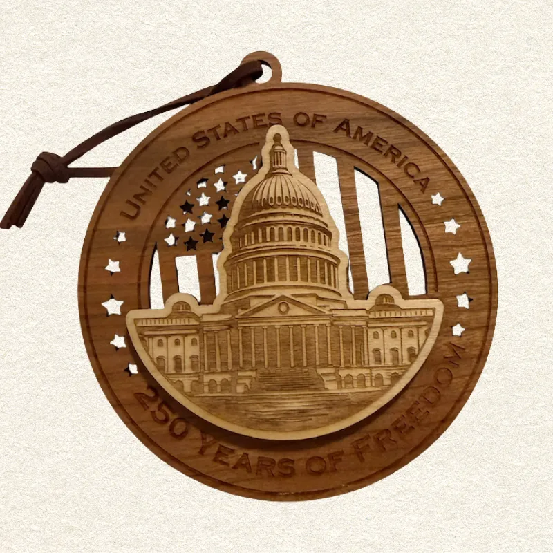 Round two-layer wooden ornament with "United States of America" and "250 Years of Freedom" engraved on the border, featuring a laser-cut flag with cut-through stripes and star field, topped with a detailed US Capitol building, hung on a brown cord